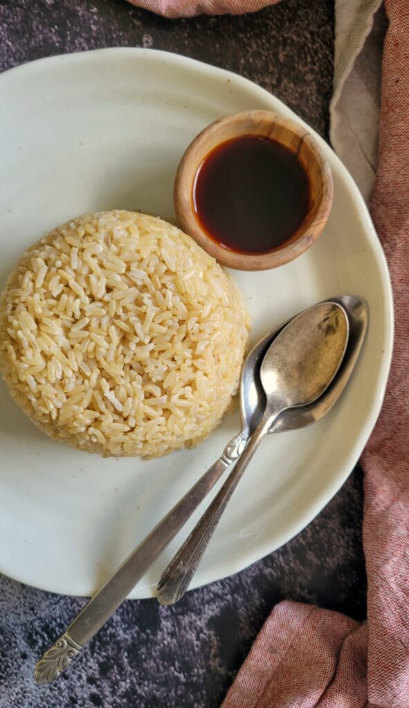 pile of brown rice on a plate with 2 spoons next to a ramekin with soy sauce
