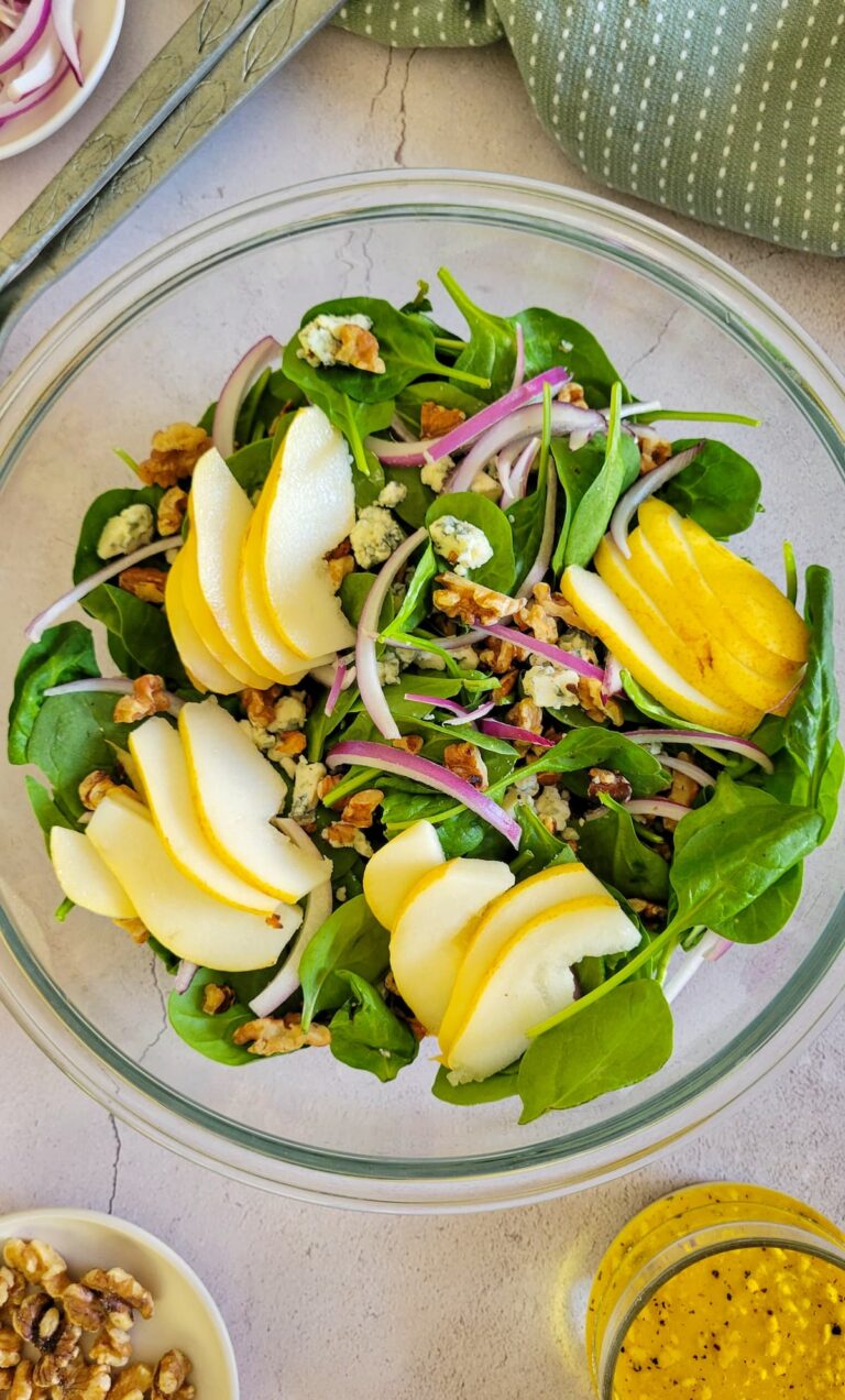 salad with pears, red onion, walnuts and blue cheese, jar of dressing in the background with a plate of walnuts and another of sliced red onions