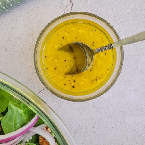 bright yellow salad dressing in a bowl with a spoon, bowl of salad in the background