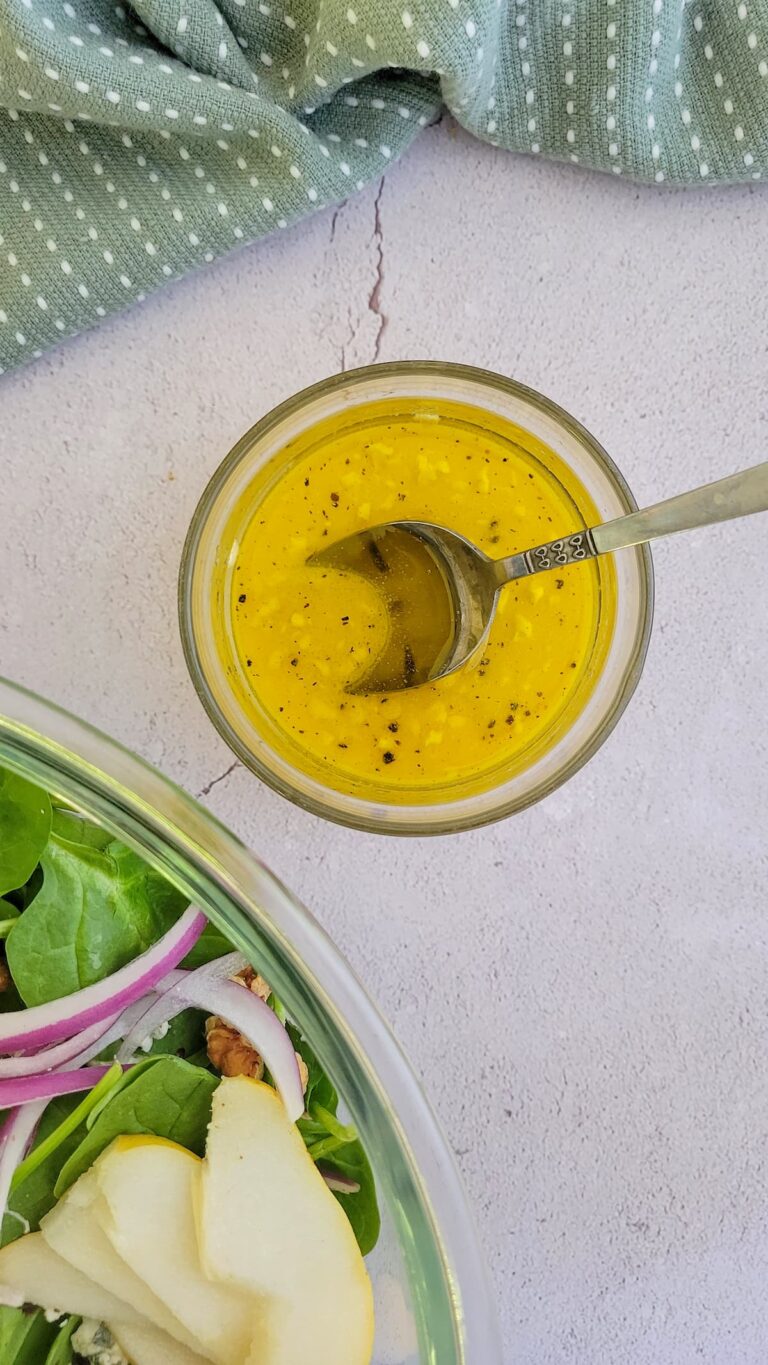 bright yellow salad dressing in a bowl with a spoon, bowl of salad in the background
