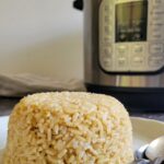pile of brown rice on a plate with 2 spoons, instant pot in the background
