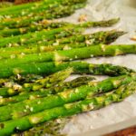 side view of roasted asparagus on a parchment lined baking sheet