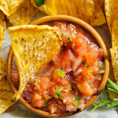 tortilla chip in a bowl of salsa, more chips around it