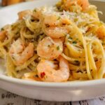 side view of shrimp pasta in a bowl with chili flakes and parmesan, garlic bread in the background