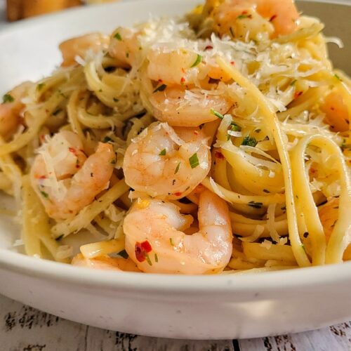 side view of shrimp pasta in a bowl with chili flakes and parmesan, garlic bread in the background