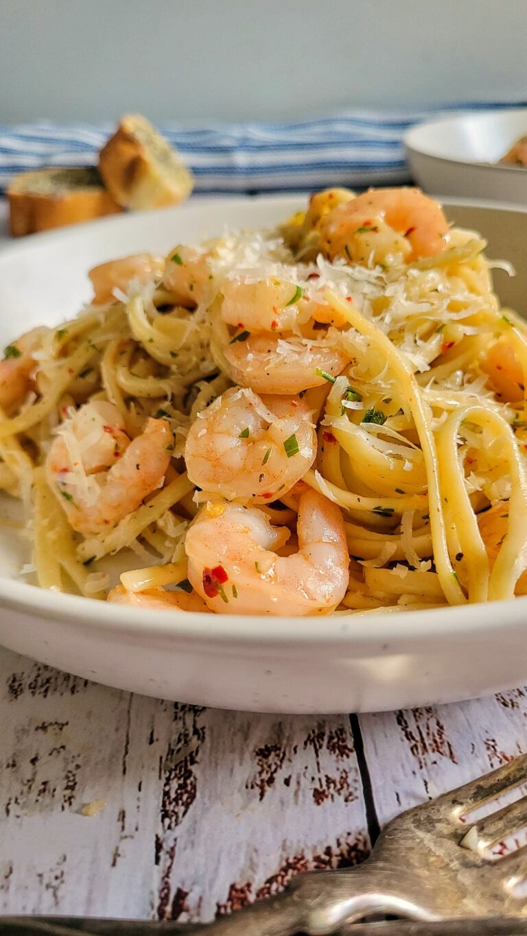 side view of shrimp pasta in a bowl with chili flakes and parmesan, garlic bread in the background