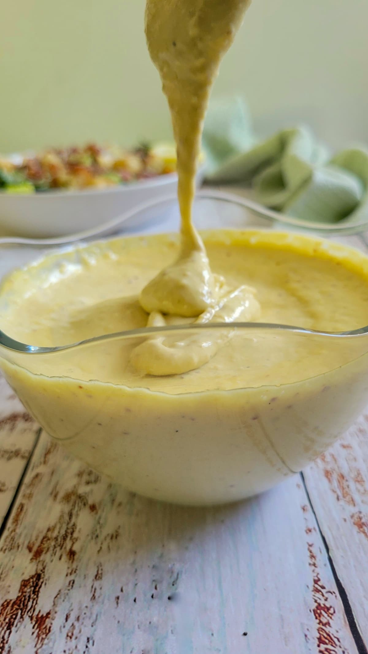 bowl of caesar salad dressing with a spoon lifting out of it, caesar salad in the background