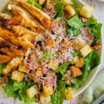 bowl of chicken caesar salad, more chicken on a plate in the background