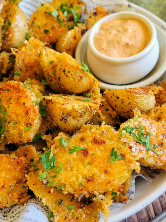 parmesan crusted baby potatoes on a plate with a bright orange dipping sauce