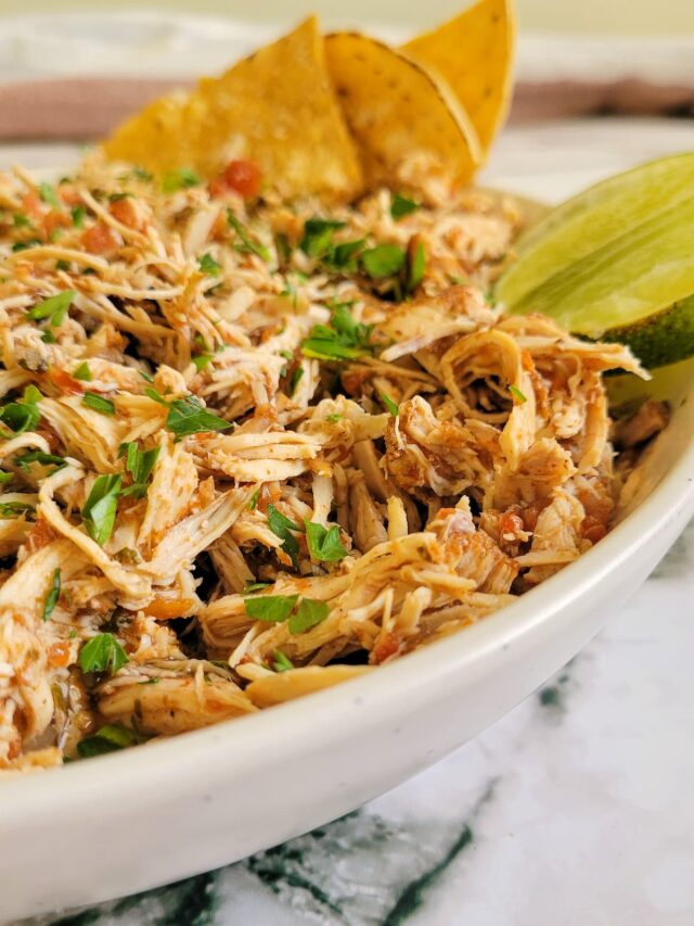 shredded salsa chicken in a bowl with fresh chopped parsley, lime and tortilla chips