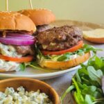 blue cheese stuffed burgers on buns on a plate with toppings, bowl of blue cheese and more toppings in the front