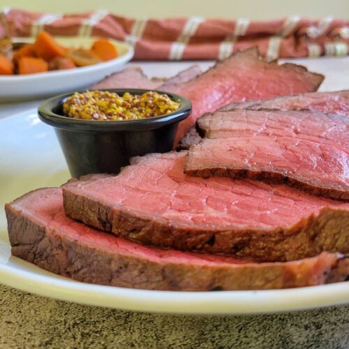 slices of medium rare roast beef on a plate with whole grain mustard