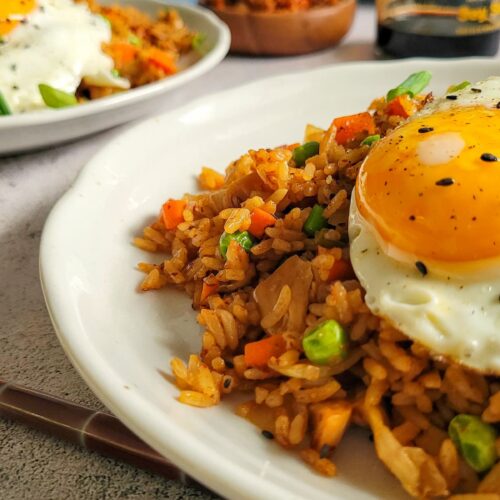 two plates of kimchi fried rice with sunny side up eggs, kimchi and soy sauce in the background
