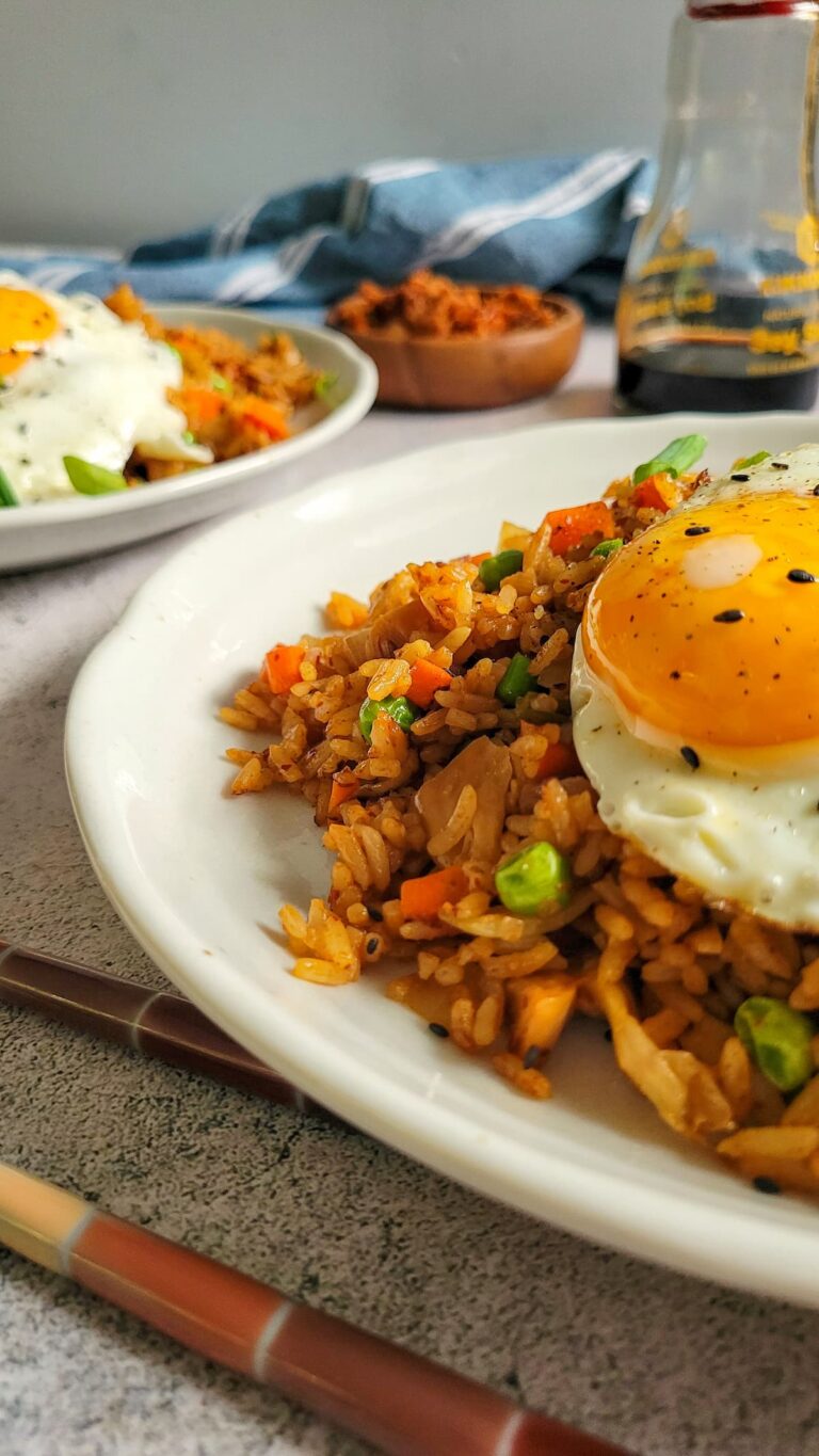 two plates of kimchi fried rice with sunny side up eggs, kimchi and soy sauce in the background