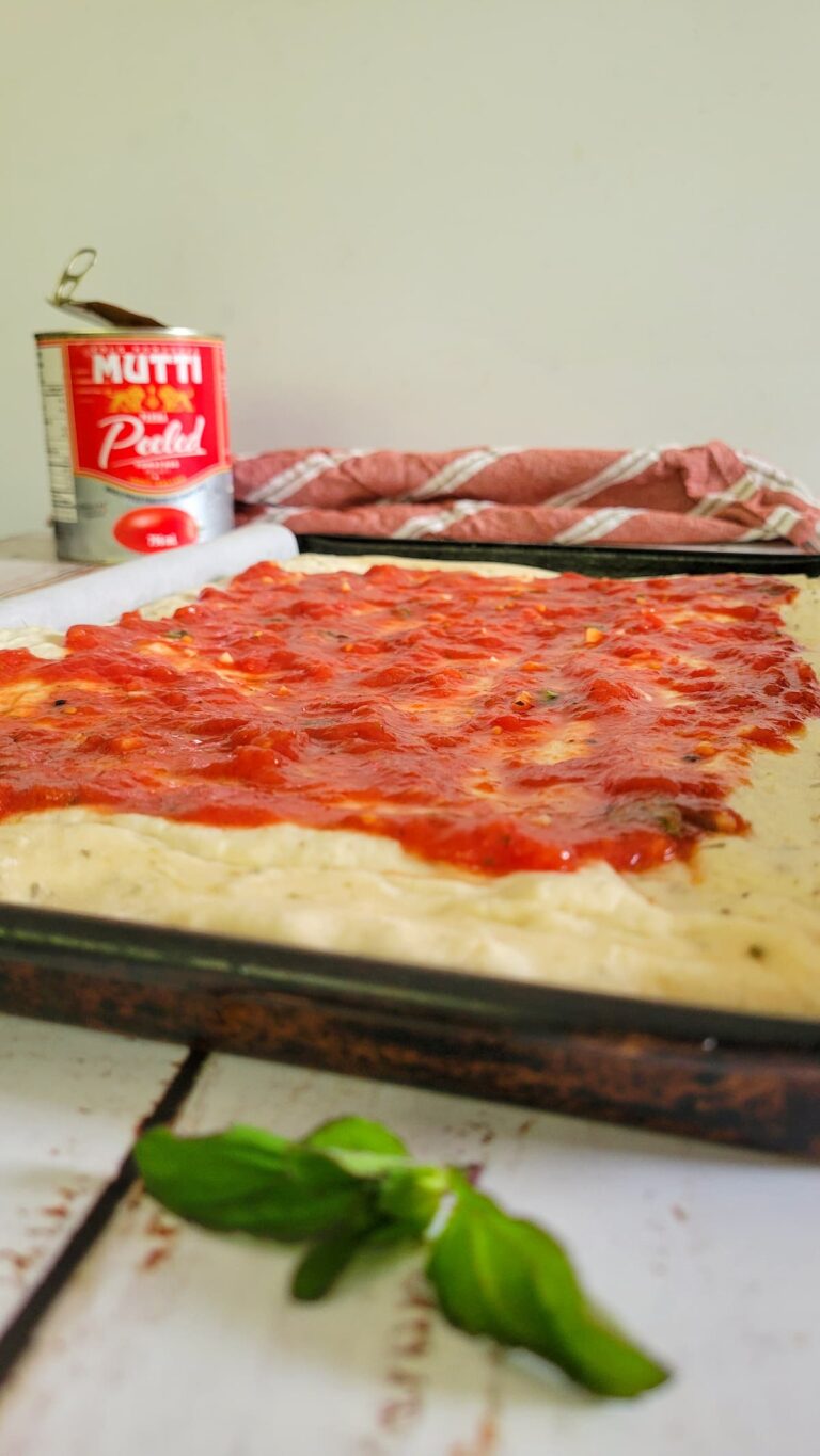pizza dough with tomato sauce, can of tomatoes in the background, fresh basil in the front