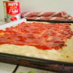 pizza dough with tomato sauce, can of tomatoes in the background, fresh basil in the front
