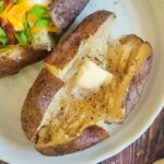 two baked potatoes on a plate, one loaded, and one with butter, salt and pepper