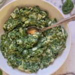 creamed spinach in a bowl with a spoon in it, raw baby spinach around the bowl