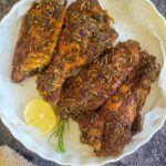 4 baked seasoned turkey wings in a dish with a lemon slice and sprig of fresh rosemary