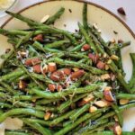grilled green beans on a plate with almond and parmesan cheese, lemon in the background