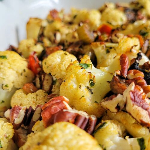 side view of cauliflower stuffing in a dish with pecans, bacon, and fresh herbs.