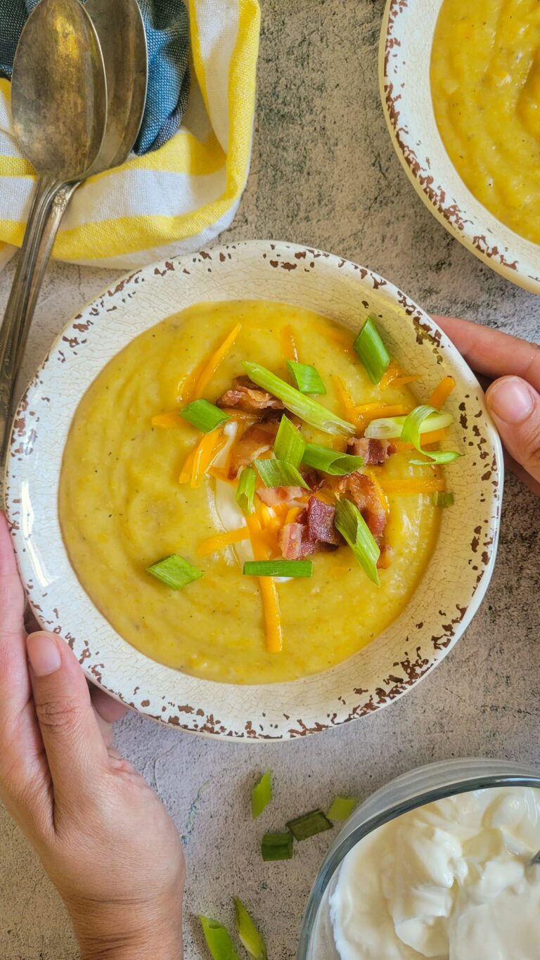 hands holding a bowl of loaded baked potato soup, bowl of greek yogurt in the background