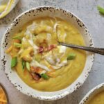 bowl of potato soup with a spoon it in, topped with green onions, bacon, greek yogurt and cheddar cheese
