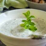 yogurt mint sauce in a bowl with a spoon and sprig of mint