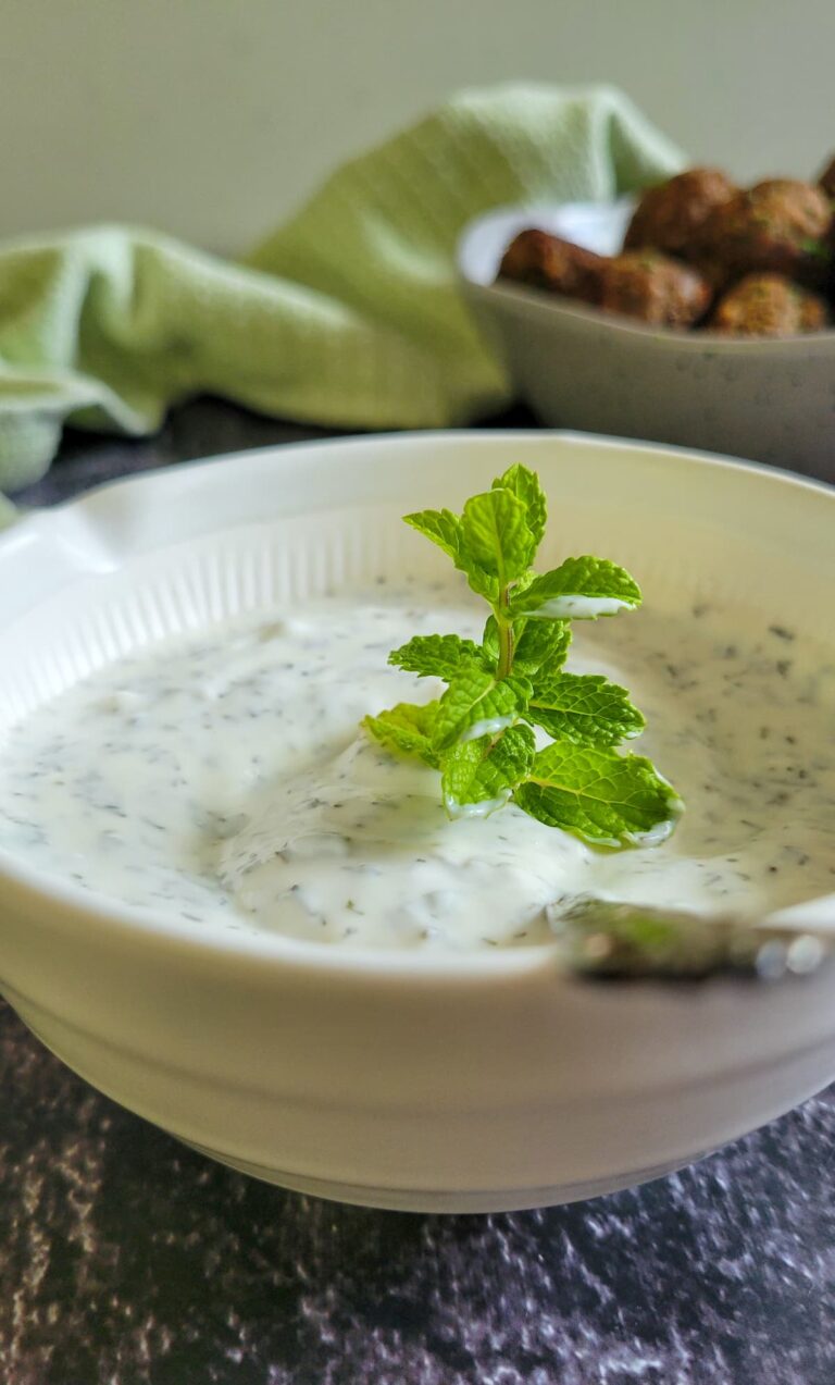 yogurt mint sauce in a bowl with a spoon and sprig of mint