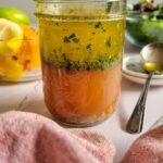 layered vinaigrette in a jar with fresh herbs, bowl of citrus peels and salad in the background