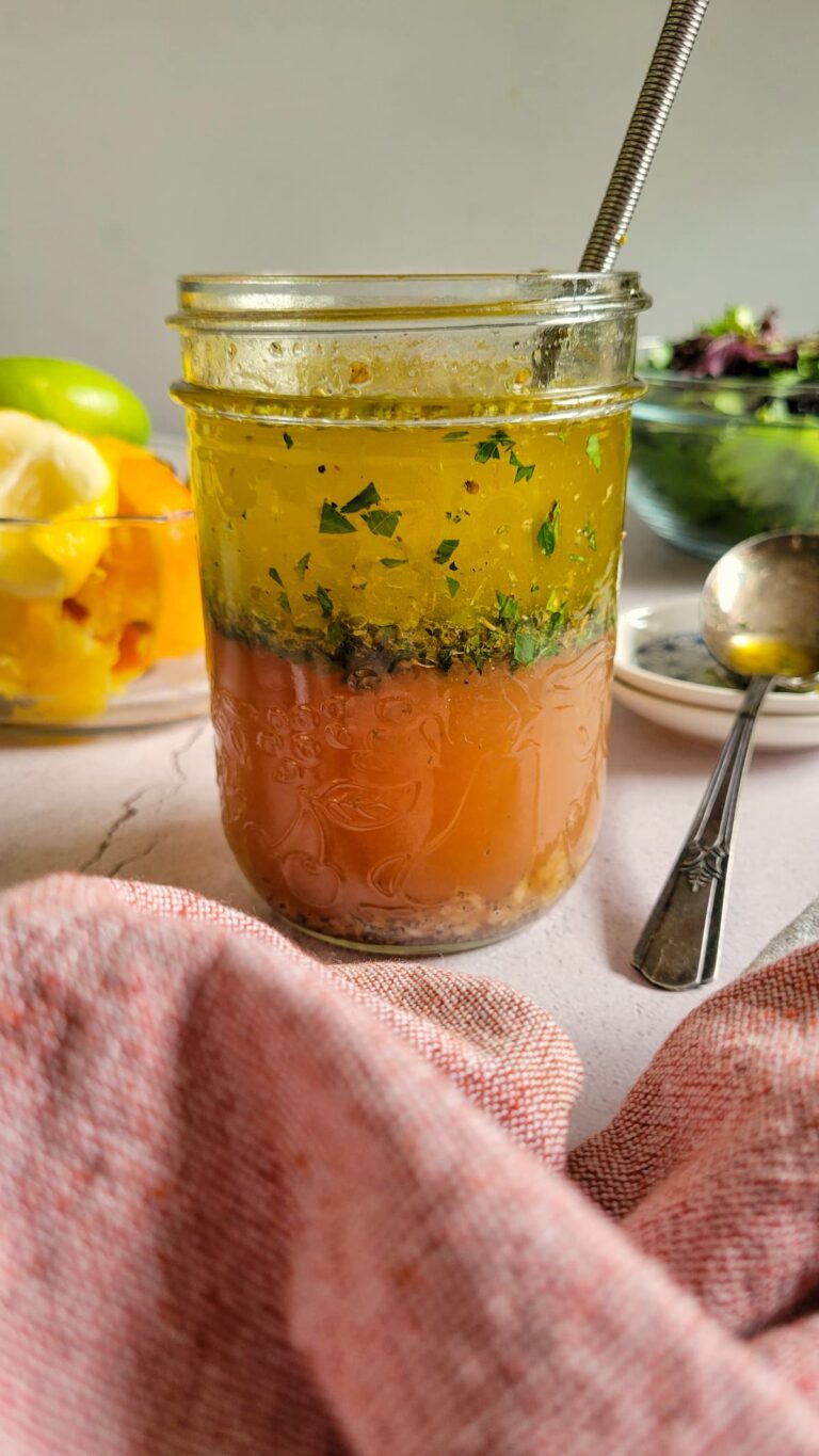 layered vinaigrette in a jar with fresh herbs, bowl of citrus peels and salad in the background