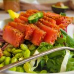 sliced tuna on a bed of greens with jalapeno and edamame, avocado and jar of dressing in the background