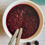 blackberry sauce in a bowl with two spoons, a few fresh blackberries in the background