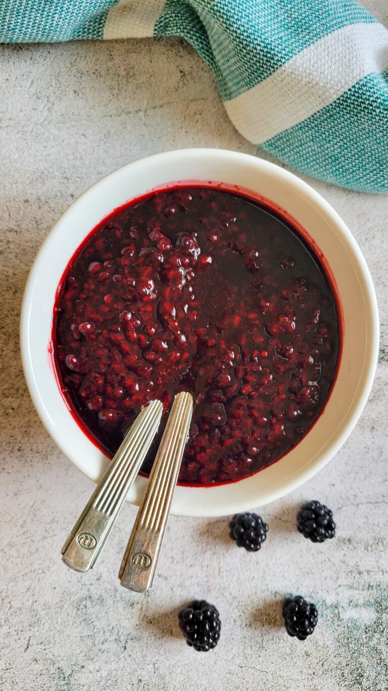 blackberry sauce in a bowl with two spoons, a few fresh blackberries in the background