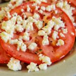 sliced tomatoes on a plate with crumbled feta cheese and fresh cracked pepper
