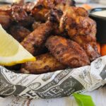 bowl of grilled chicken wings with green onions, lemon, and a creamy white sauce
