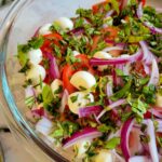 sliced red onions, fresh chopped basil, mini mozzarella cheese balls, and quartered tomatoes unmixed in a bowl