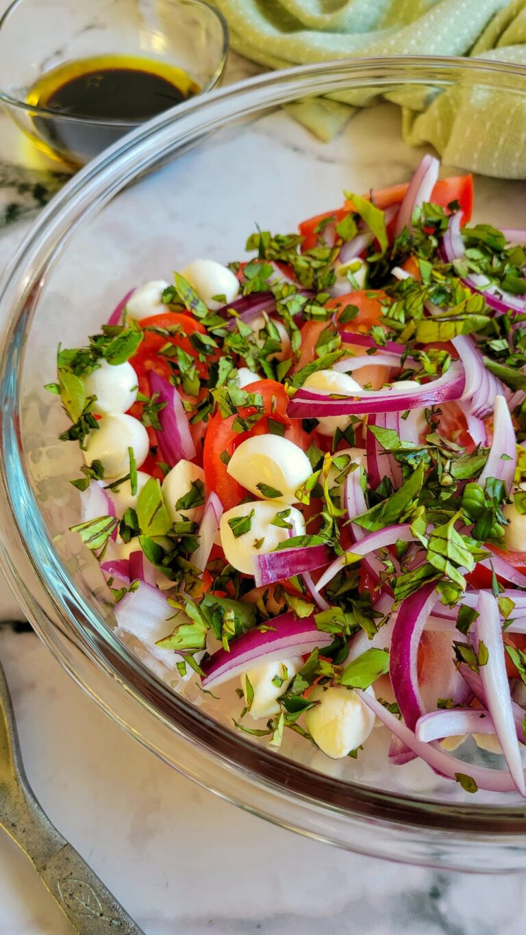 sliced red onions, fresh chopped basil, mini mozzarella cheese balls, and quartered tomatoes unmixed in a bowl