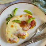 cauliflower steak with mozzarella, tomato sauce, and basil on a plate with a fork and knife, another on a plate in the background
