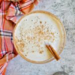 creamy martini in a martini glass with a cinnamon stick and powdered cinnamon on top next to a martini shaker