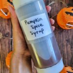 hand holding a squeeze bottle with pumpkin spice syrup over a few pumpkins in the background