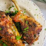 3 roasted seasoned turkey drumsticks on a plate topped with fresh chopped parsley.
