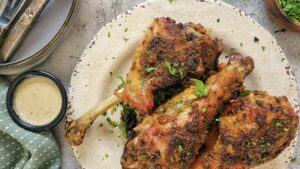 3 cooked turkey drumsticks on a plate with fresh chopped parsley, ramekin with white sauce next to it with plates and forks.