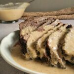 sliced beef on a plate with pale brown gravy over top. Gravy boat with more in the background
