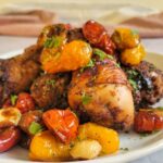 plate of chicken drumsticks with tomatoes and garlic garnished with fresh chopped parlsey