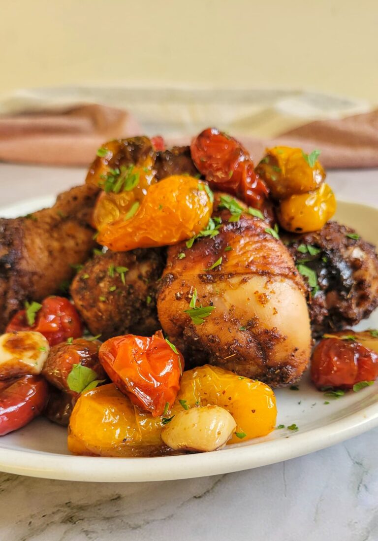 plate of chicken drumsticks with tomatoes and garlic garnished with fresh chopped parlsey