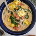 bowl of tortellini soup with cream, spinach, tomatoes, and parmesan cheese