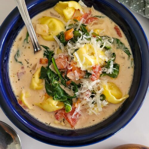 bowl of tortellini soup with cream, spinach, tomatoes, and parmesan cheese