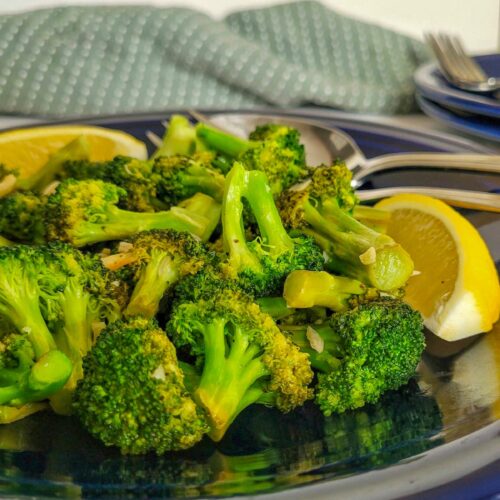 cooked broccoli on a dark blue plate with sliced lemons.