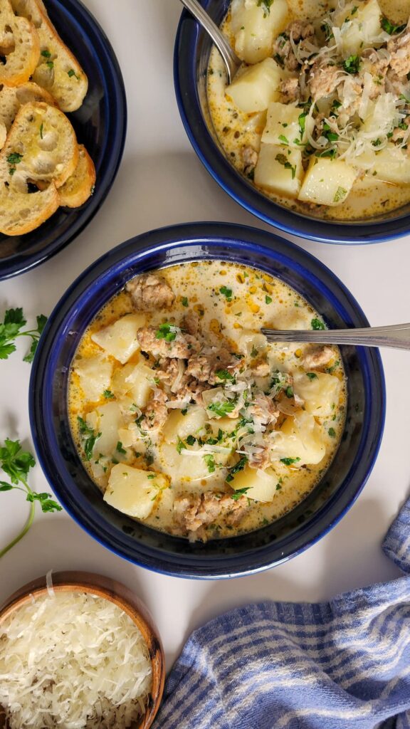 bowls of sausage and potato soup with fresh chopped parsley next to a plate of crostini